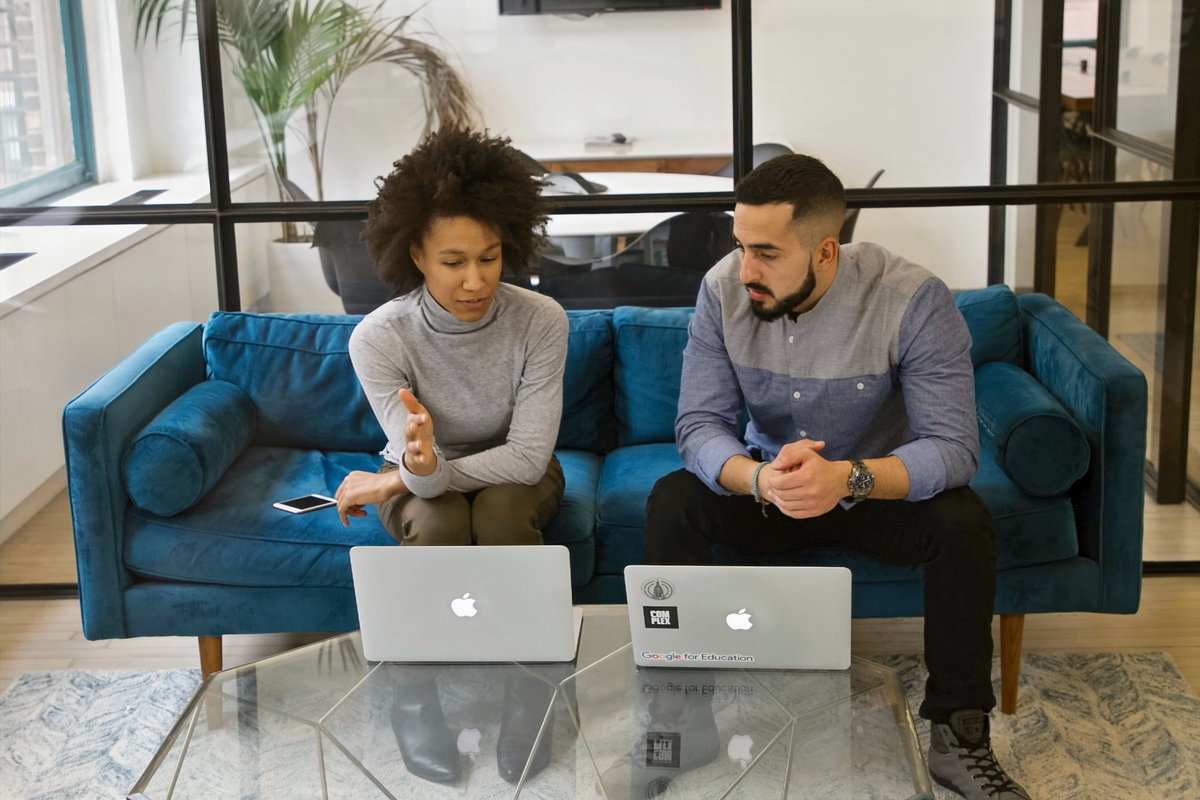 Two colleagues talking over laptops in an office.