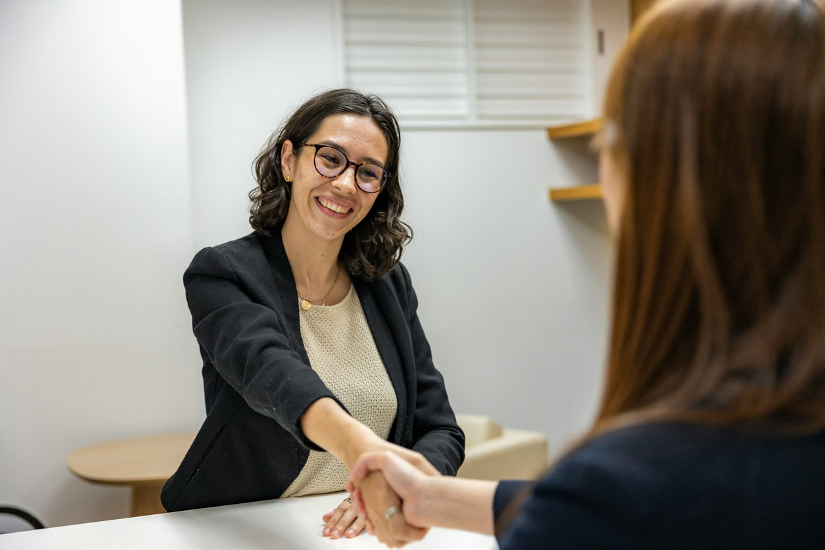 Two people shaking hands across a desk at the end of an interview.
